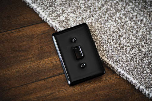 A photo of the Metro glazed black decorative ceramic wallplate on a wood table and a textured blanket