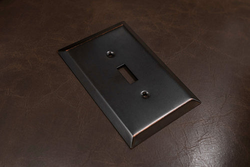 A photograph of the Oversized aged bronze metal wallplate laying on a brown leather background