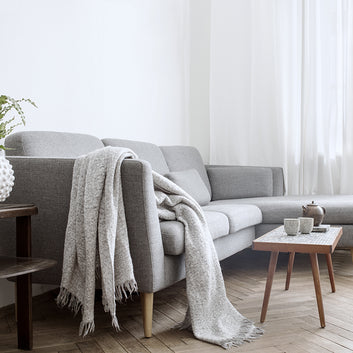 An interior photo of a professionally designed Scandinavian decor style living room with a gray couch, a soft blanket, and white window drapes