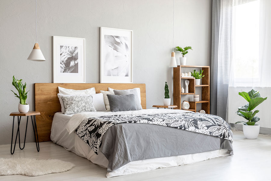 A Scandi decor style bedroom with light wood floors, grey walls, minimalistic nightstands, a large window, a wooden bookshelf, and soft grey bedding