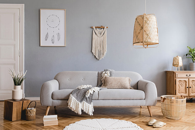 A Bohemian decor style living room with wood floors, grey walls, bohemian style wall decorations, and a minimalistic grey fabric couch