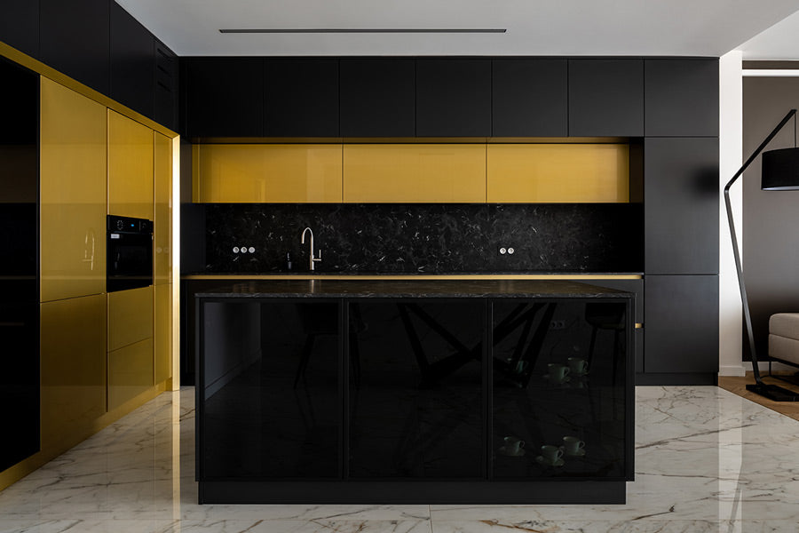 A professionally designed Hollywood Regency Glam kitchen with black marble countertops, black walls, white granite floors, and bold gold cabinetry