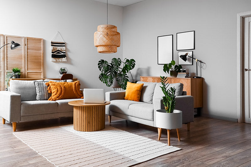 A Scandinavian decor style living room with functional minimalistic couches, coffee tables, and cabinetry, and with grey walls, wood floors, vibrant yellow pillows, and lots of green plants