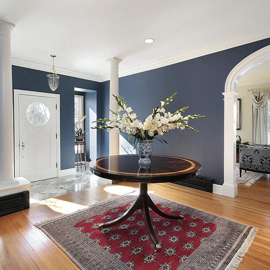 An interior photo of a professionally designed Traditional decor style entryway with a blue walls, white columns, a decorative red rug, and a wood table with flower on it in the center of the room