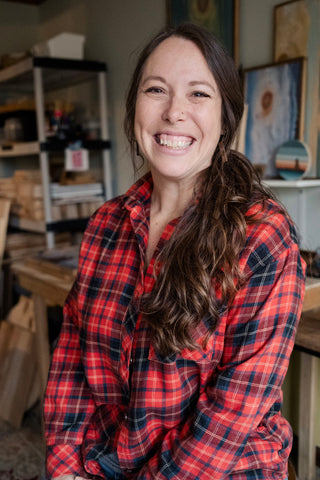 Erin smiling happily in her studio wearing a red plaid shirt.