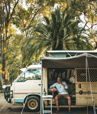 Man sitting in a van with his awning up drinking a coffee