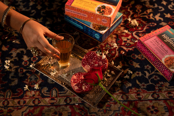 Hand holding tea on platter with pomegranate on a tablescape with House of Kajaana meals. 