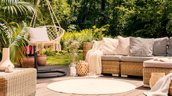 Outdoor patio with rattan sofa and accent chairs, swing chair, round are rug, pillows and throws and accent decors, with greenery and forest background