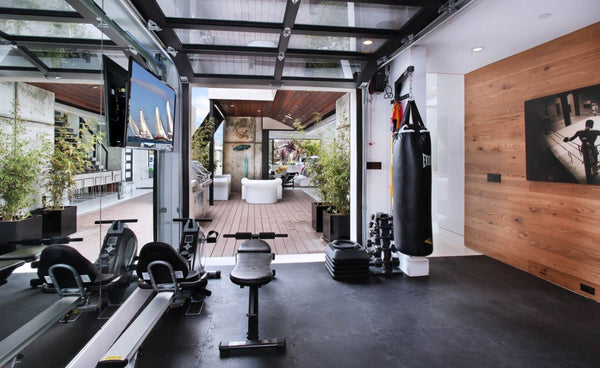 Home gym showing garage pull up door, fitness equipment, wood accent wall with led tv, rubber floor