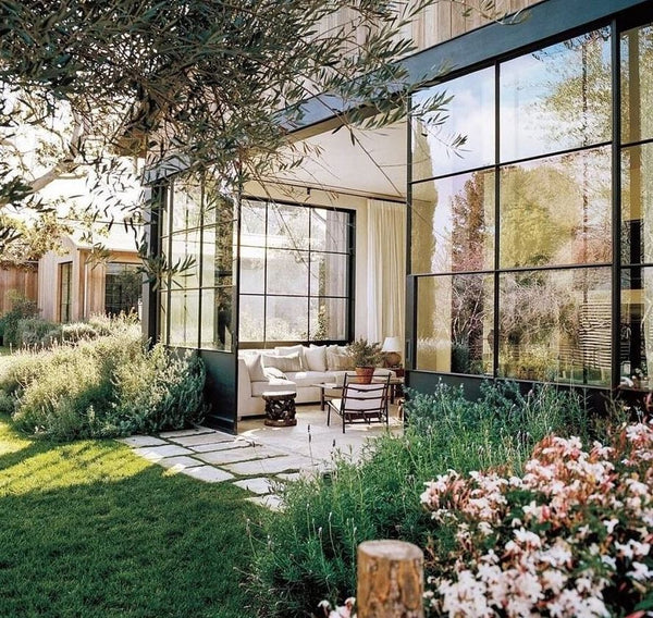 Green home with different plants and landscaping exterior, glass windows and doors with upholstered white sofa and accent chair