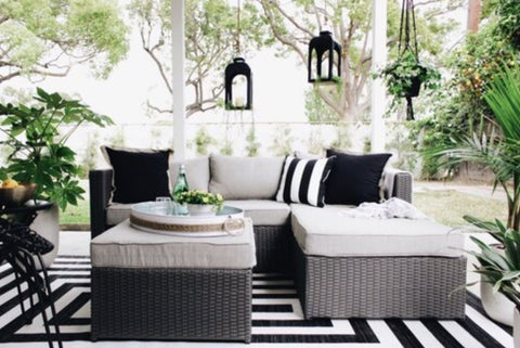 Patio with black and white outdoor furniture, accent rug, pillows and throws, plants and background greeneries 