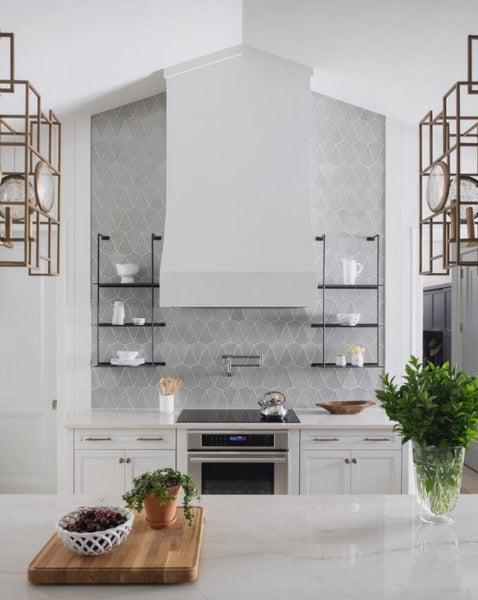 Modern kitchen with grey decorative patterned backsplash, metal shelving, white shaker type cabinet, pot filler and huge white range hood