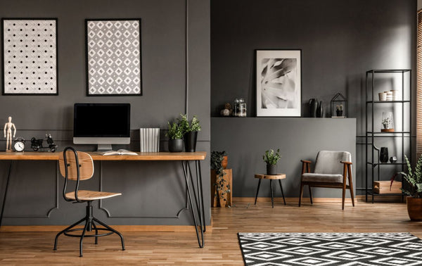 Home office with dark grey painted walls, wall artworks, office tables, office chair, lounge chair, bookshelves and wood plank floor