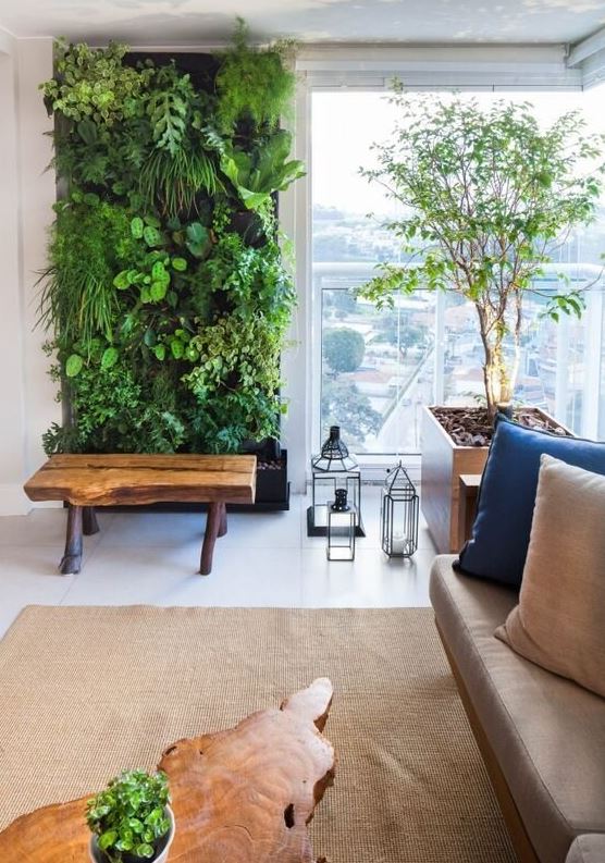 Living area with green wall, sofa with blue and cream pillows, brown are rug, potted plants and wooden bench