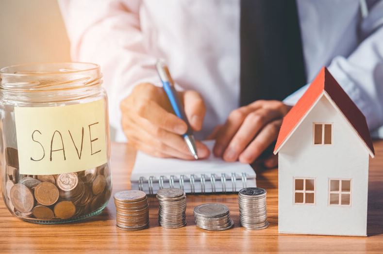 Saving for you dream house with wood table, coins, money, house scaled model and hands writing on a notebook