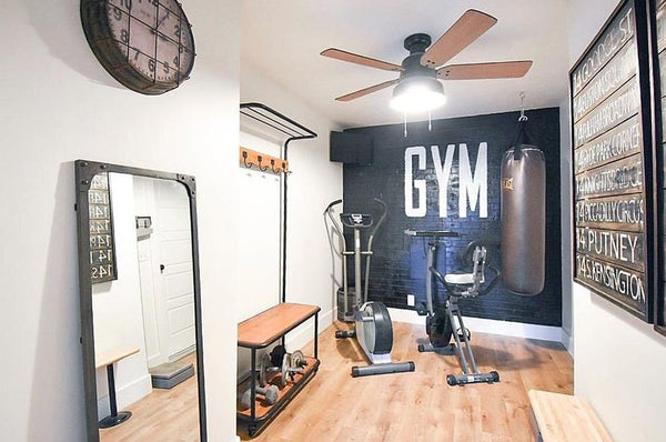 Home gym with fitness equipment, ceiling fan, mirror, clock, black brick wall and wooden floor planks