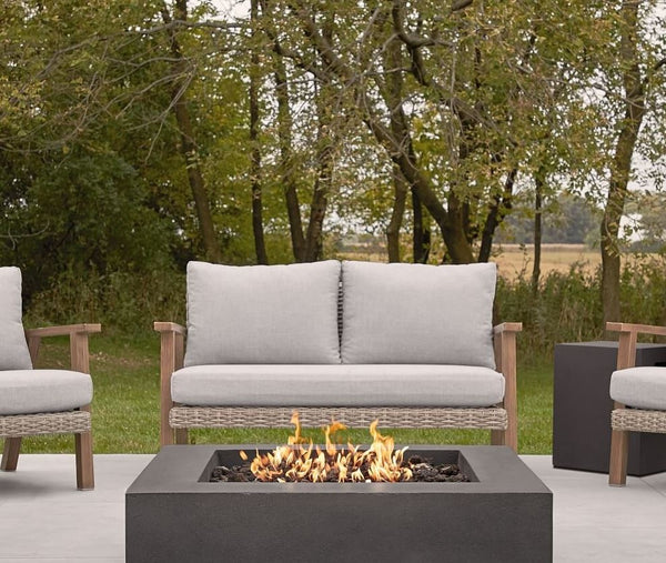 Outdoor fire pit with concrete floor, wicker sofa with upholstered back and set, farm and forest background