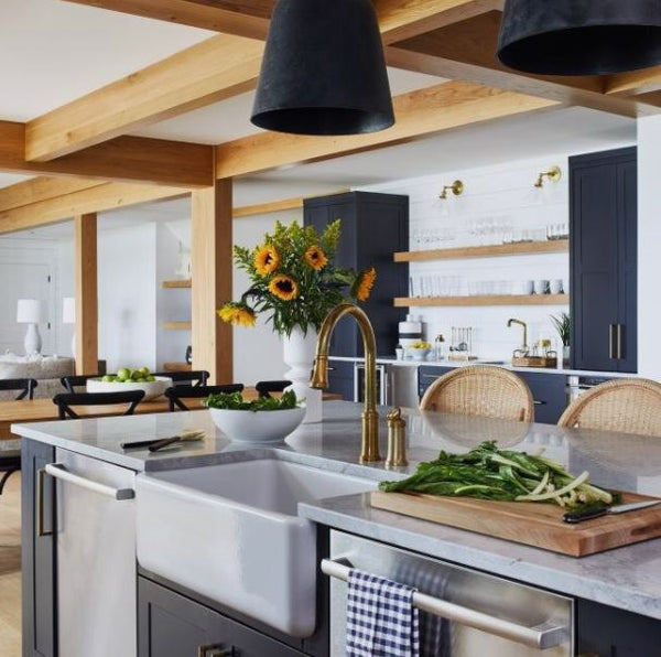 Farmhouse kitchen with farmhouse type sink, black pendant lights, wood beam ceiling, black laminate cabinet and gold faucet