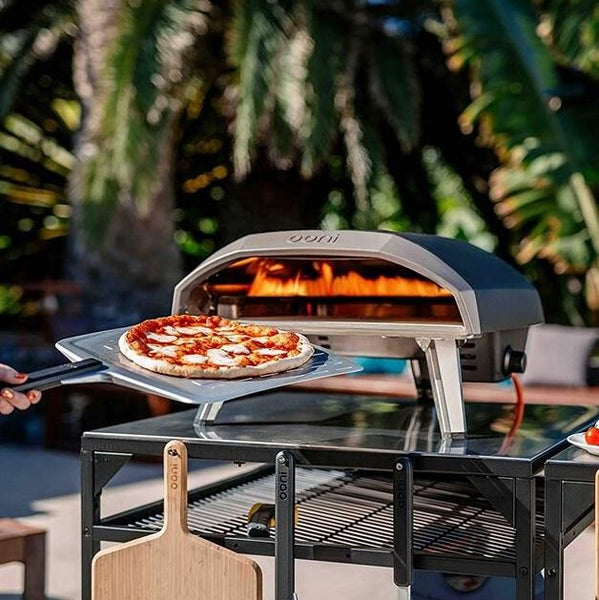 Outdoor pizza oven with metal rack stand, pizza cooking, greenery background