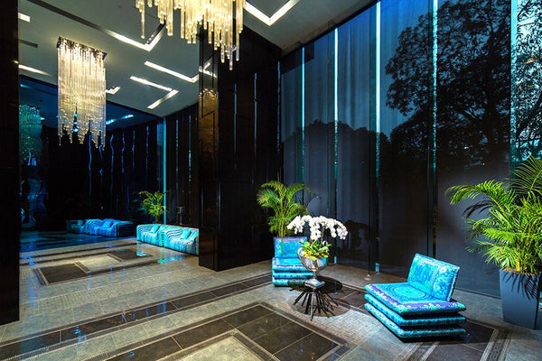 Century properties in the Philippines called The Milano Residence showing a lobby with Versace furniture and decors with marble floor printed blue sofa and lounge chairs vertical glass chandeliers palm indoor plants high ceiling lobby