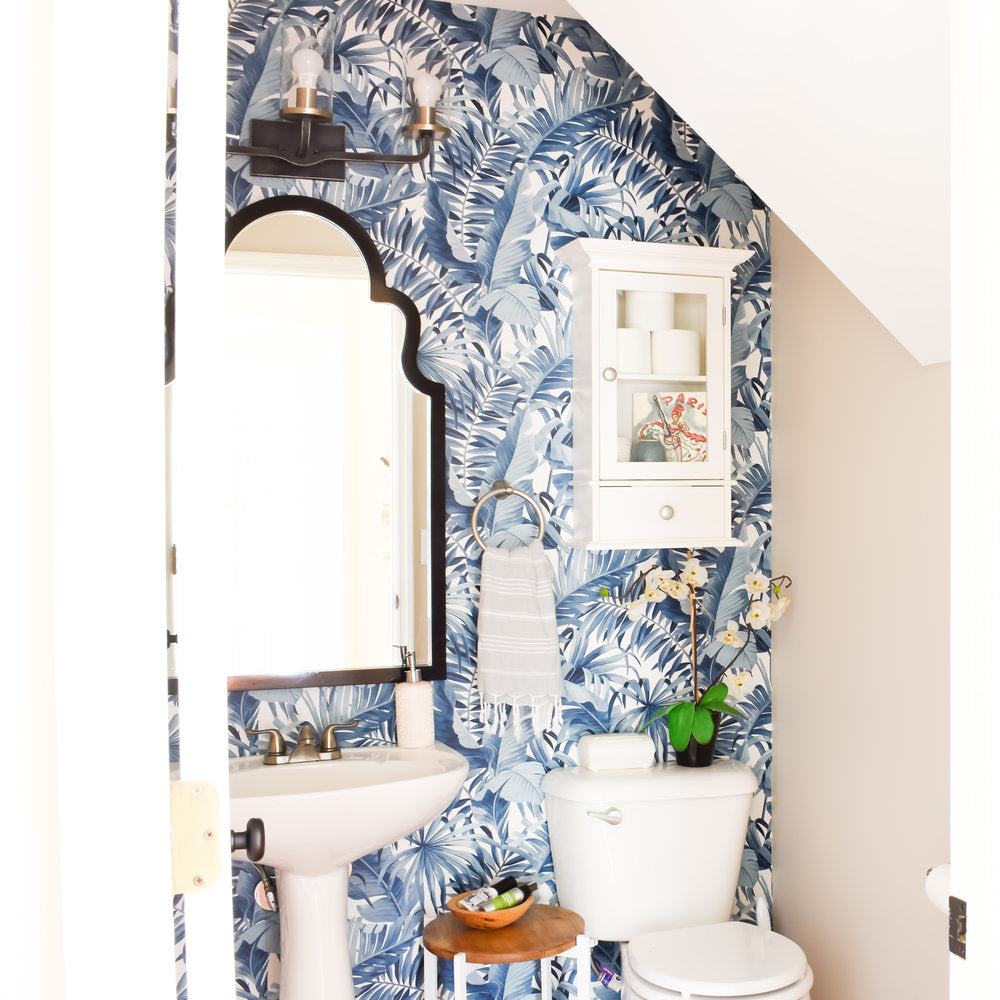 powder room interior design with blue tropical palm leaf wallpapers, medicine cabinet, white plumbing fixtures, vanity mirror and lights