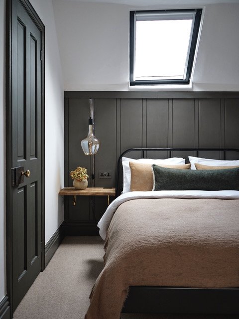 bedside table showing bedroom with wainscoting in dark grey paint and black door with gold handle, glass sconce lighting fixture 