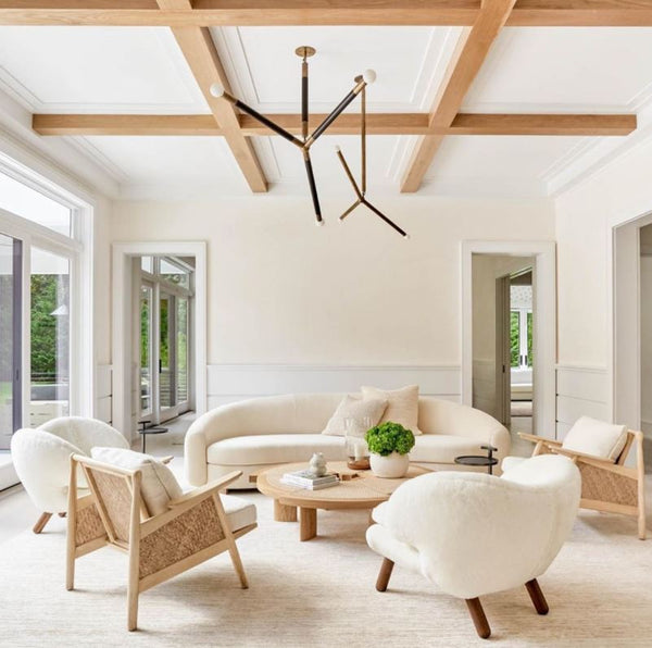 Living area with upholstered puffy sofa and accent chairs white wall wood beam ceilings modern metal chandelier and white are rug