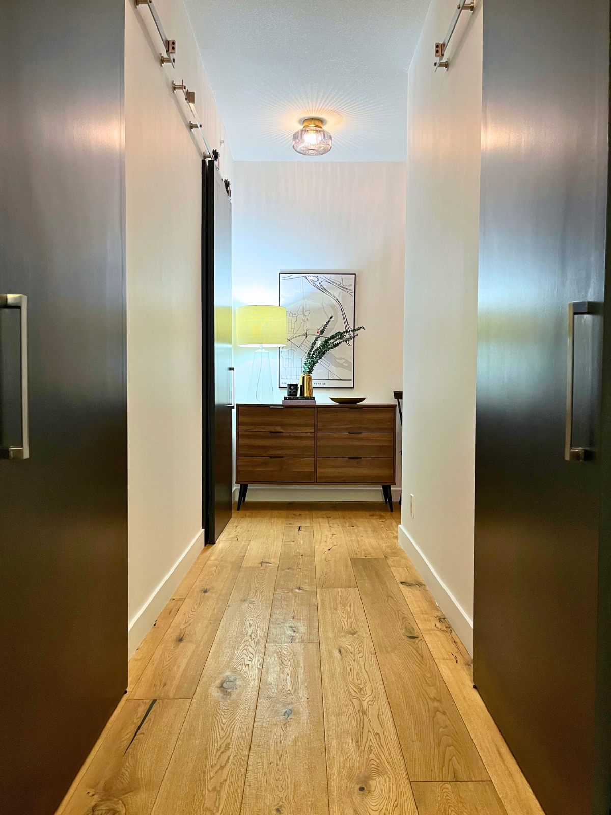 newly transformed hallway with white painted walls, black barn doors, wooden console table and hardwood flooring