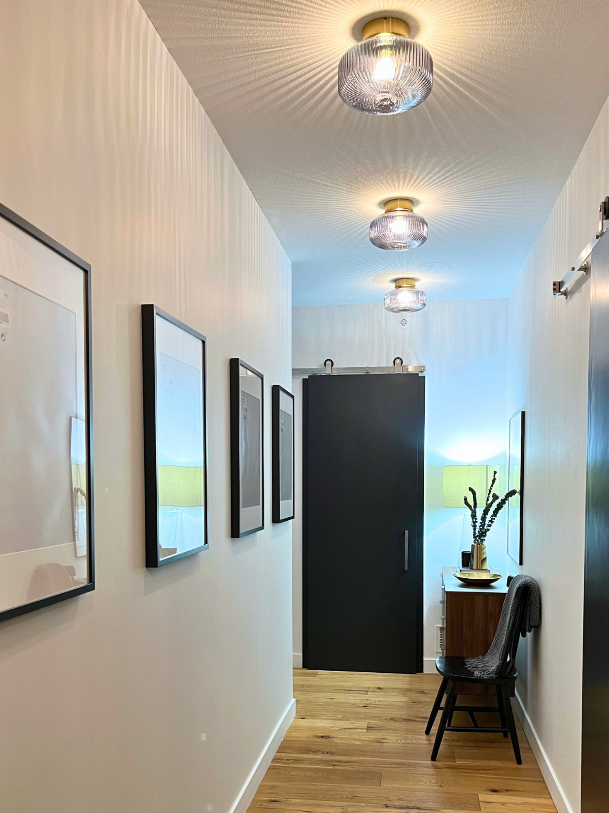 renovated hallway with flush mounted decorative light fixtures, hardwood flooring, white painted walls and black barn doors