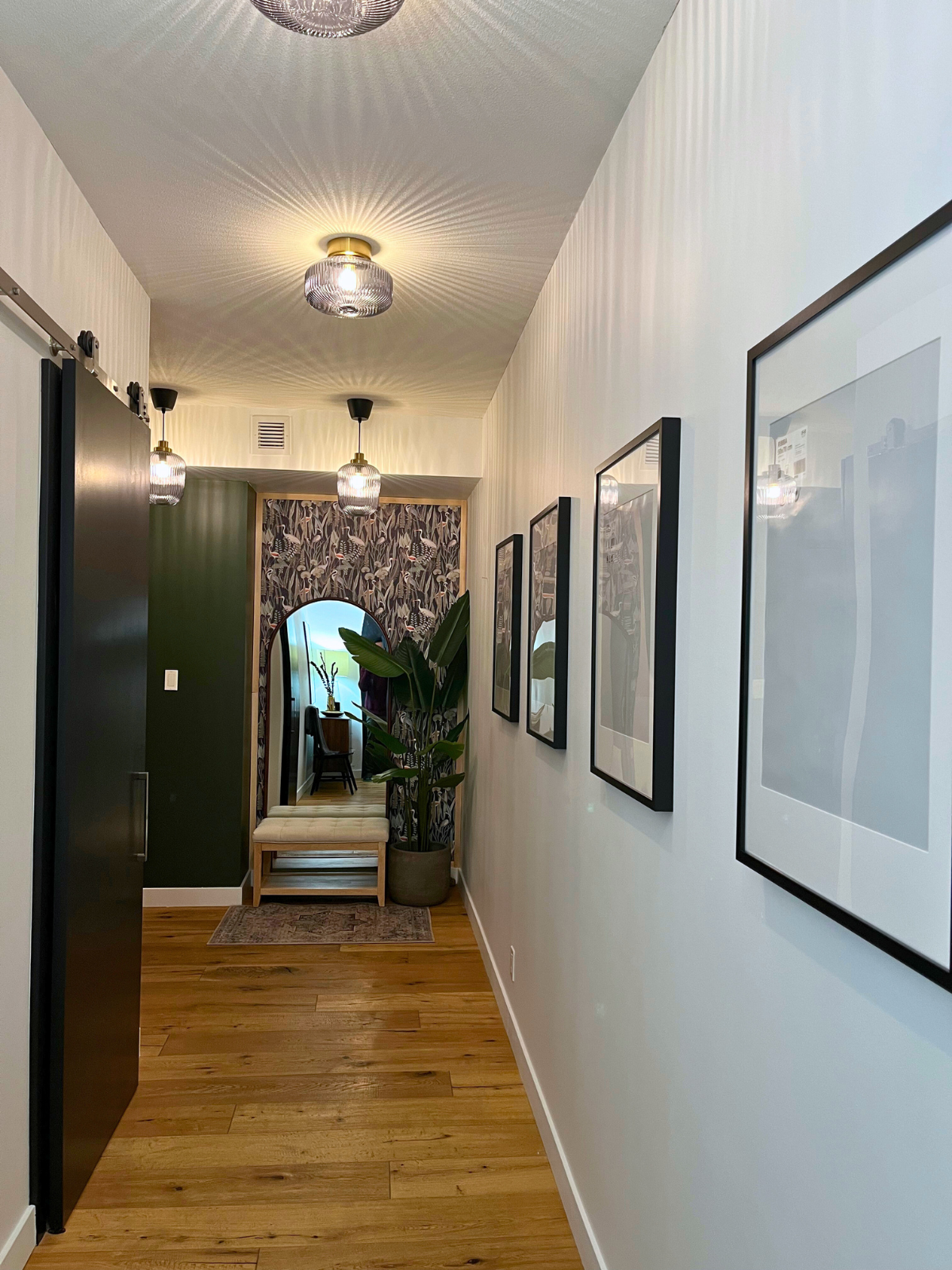 hallway with gallery wall, white painted walls, black barn doors, existing hardwood flooring and flush mount decorative light fixtures