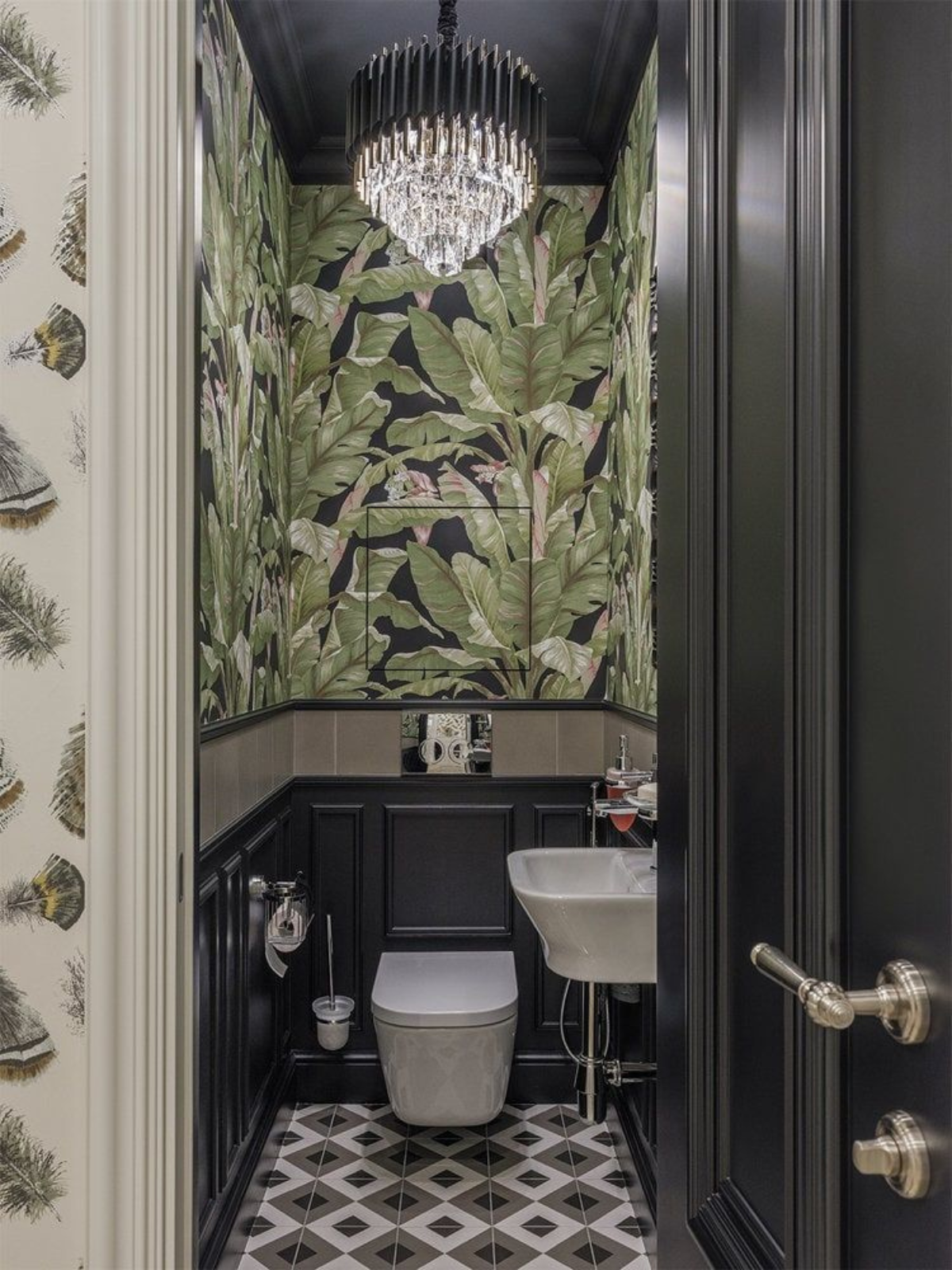 powder room with tropical inspired wallpaper, crystal chandelier, patterned tile flooring, toilet and vanity sink