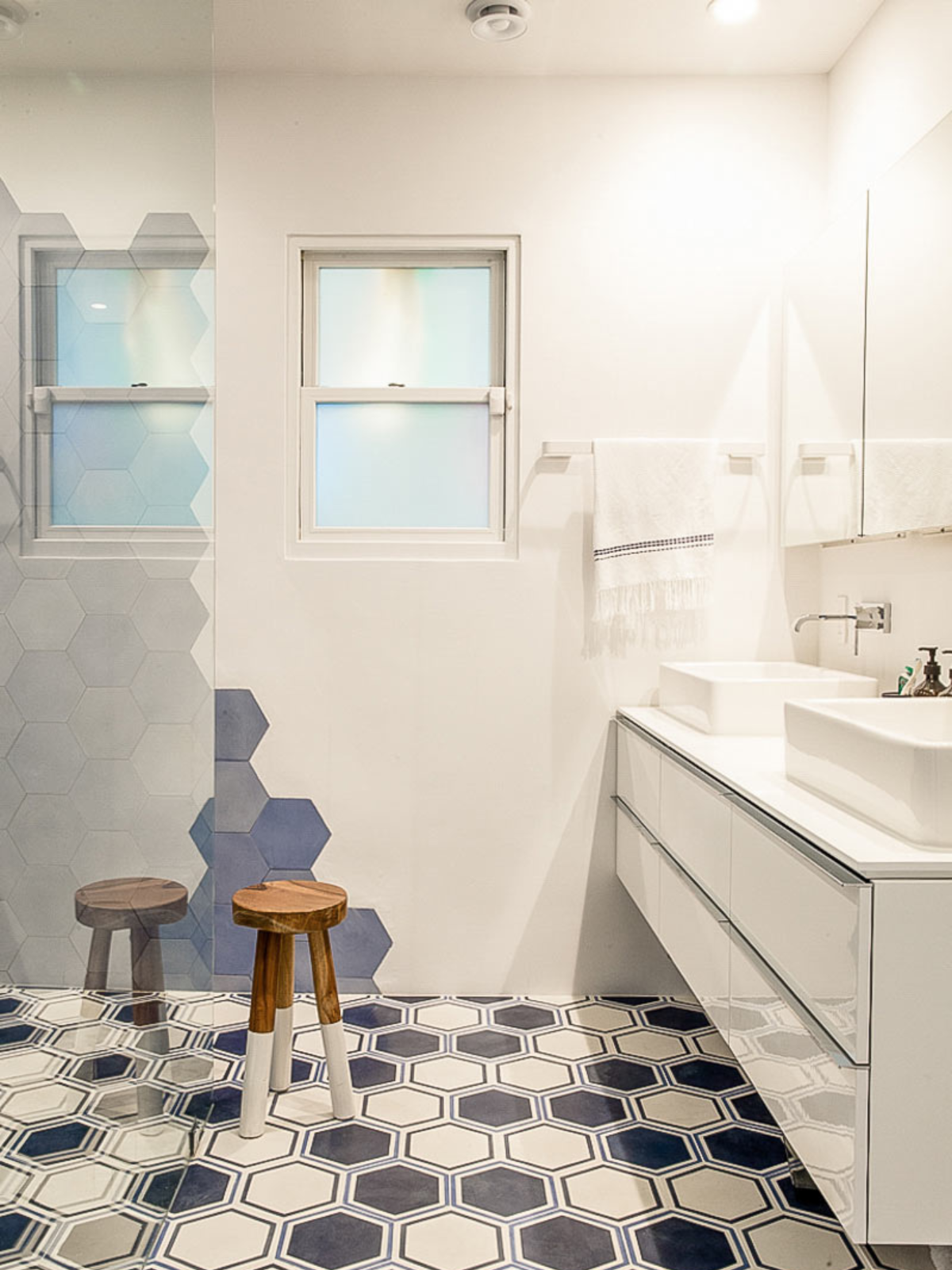 bathroom showing balck and white mosaic tiles flooring, a round bench, glossy modular vanity cabinet, white painted walls and simple window