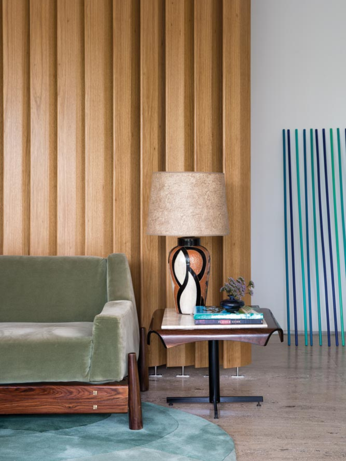 living room showing vertical accent wood panels, green upholstered couch, table lamp and blue area rug
