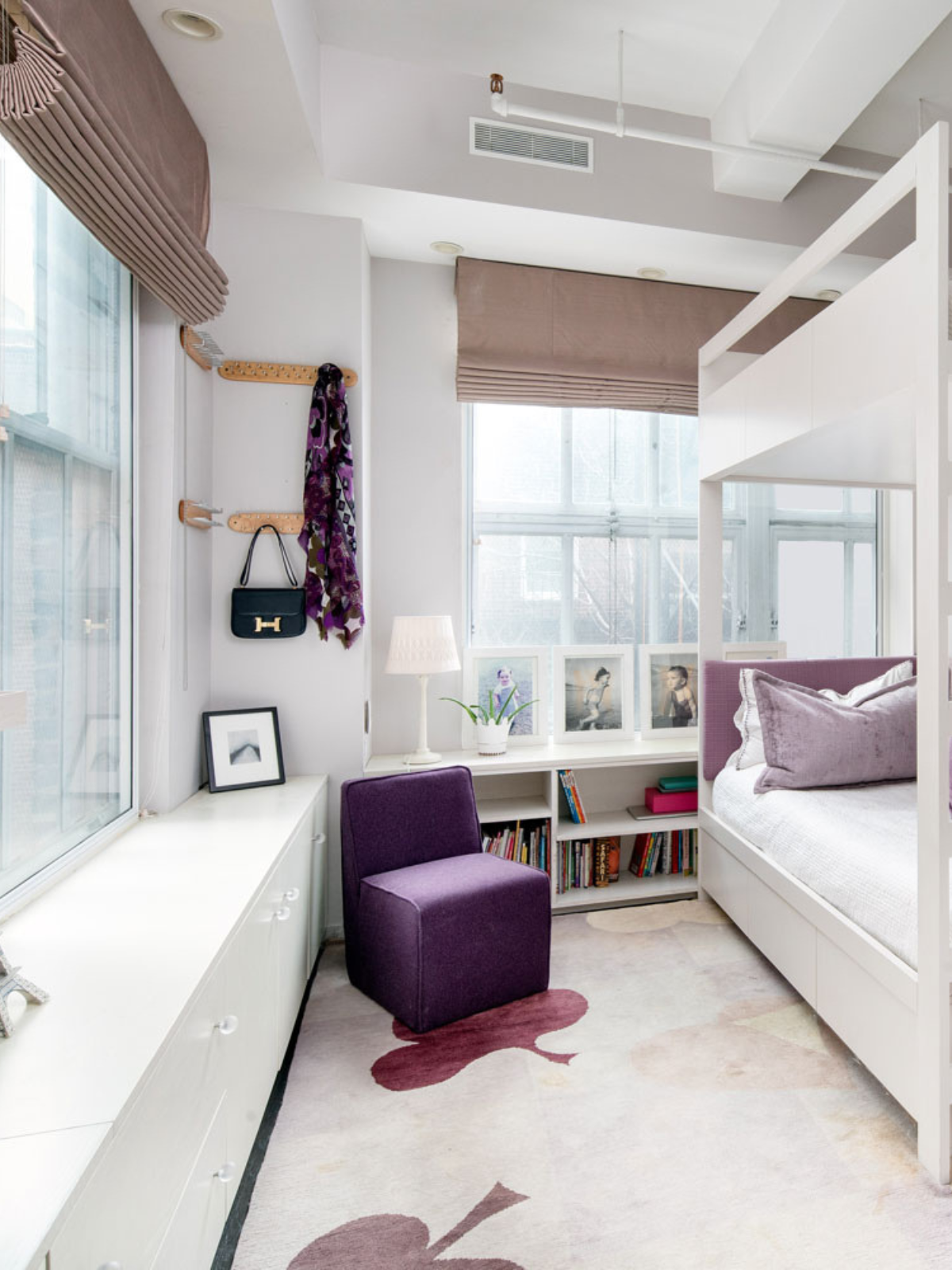 a chic looking bedroom with white bed, purple pillow accents, purple upholstered accent chair and brown fabric window shade
