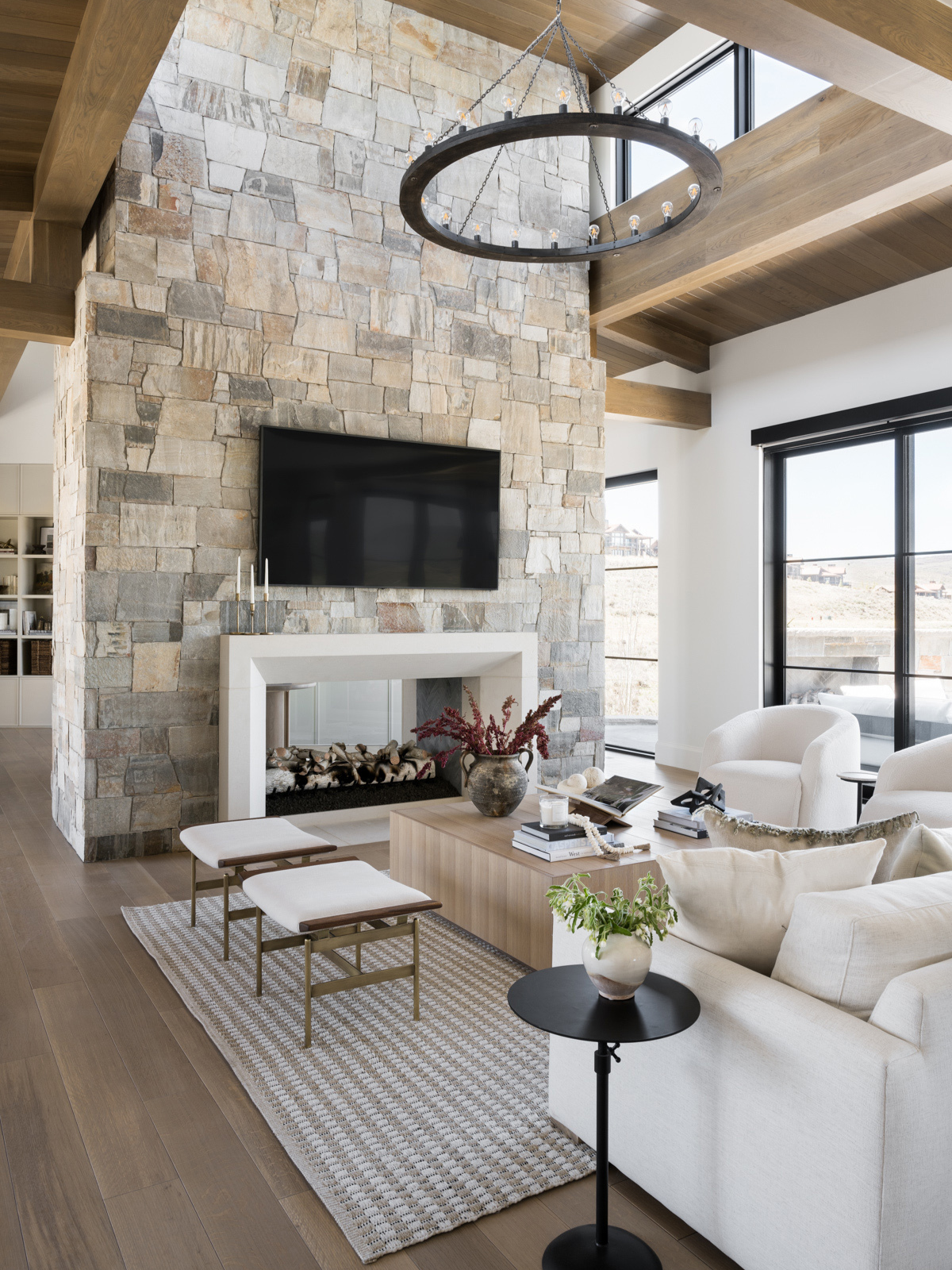 a living room showing giant fireplace with stone finish, wooden flooring finish, white upholstered couch and round chandelier