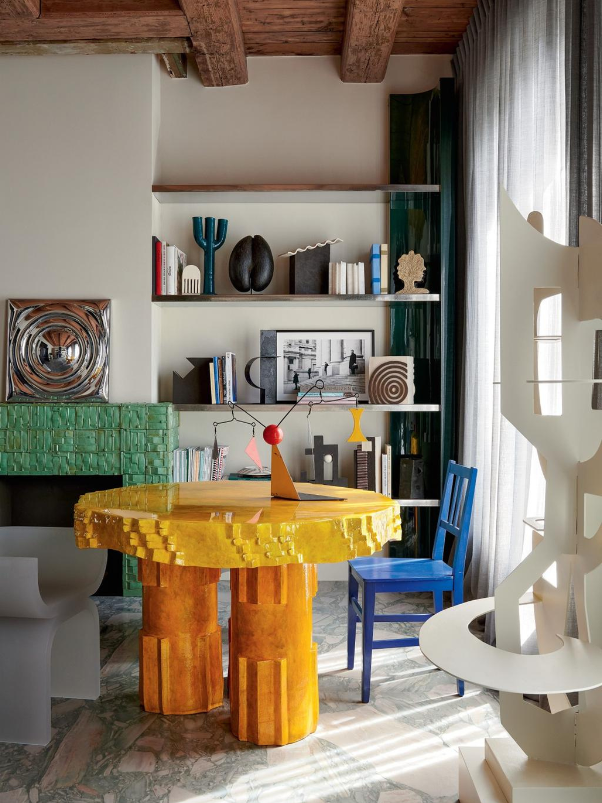 home library and reading area showing yellow accent table and accent chairs in vibrant colors, shelvings in the background, wooden ceiling and stone flooring