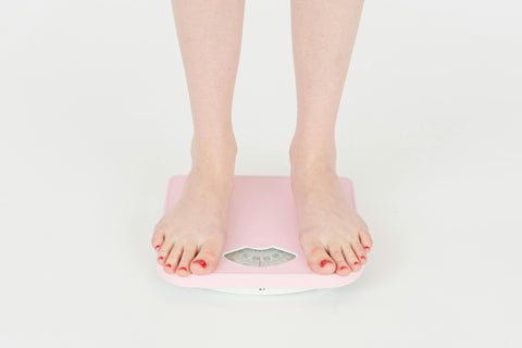 A close-up of a person's bare feet with painted toenails standing on a pink bathroom scale.