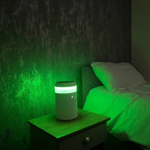 A Demi Air Purifier sitting on a bedside table giving off a strong green light in a darkened bedroom