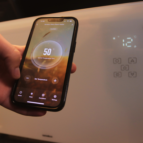 A photo of the Senelux Wifi Panel Heater with a mobile phone showing the temperature and controls, indicating smart app control