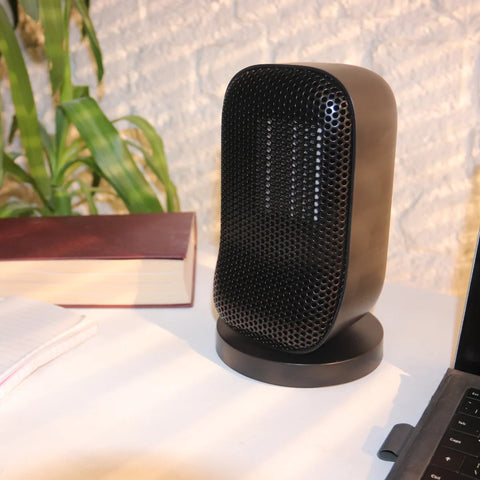 A photo of the Senelux Desktop Space heater on a white desk with a laptop on the right and a book on the left