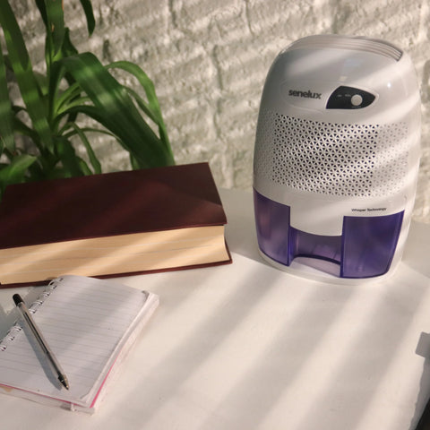 A photo of a Senelux Mini Dehumidifier sitting on a white office desk with a notepad and pen next to it