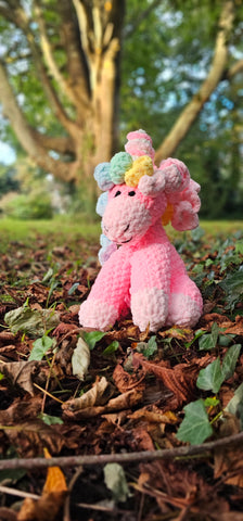 A stuffed and knitted pink unicorn sits in a pile of leaves with an ancient oak tree in the background