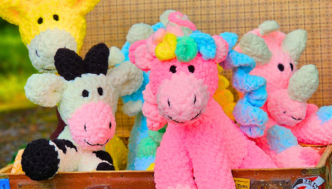 5 brightly coloured stuffed toys seen in vintage suitcase. A stuffed unicorn, cow, giraffe and pink dinosaur are seen