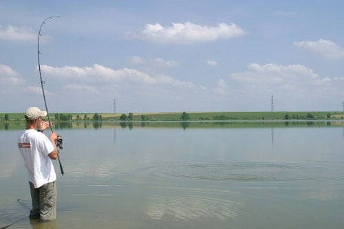 A man in still water, holding a fishing rod.