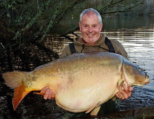 Andrew smiling whilst holding a massive carp he caught whilst fishing.