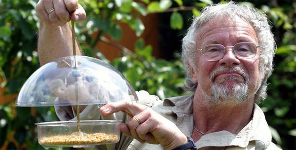 Bill Oddie holding a bird feeder filled with bird food.