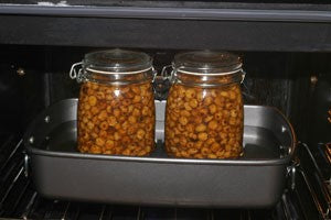 Two filled jam jars on a baking tray, in an oven.