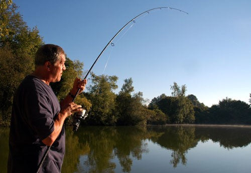 Ken holding his fishing rod next to a still fishing lake.