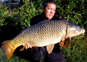 Ken holding a large carp, in a sunny spot.