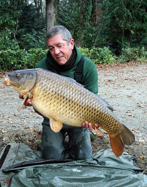 Ken wearing a green jumper and holding a large carp.